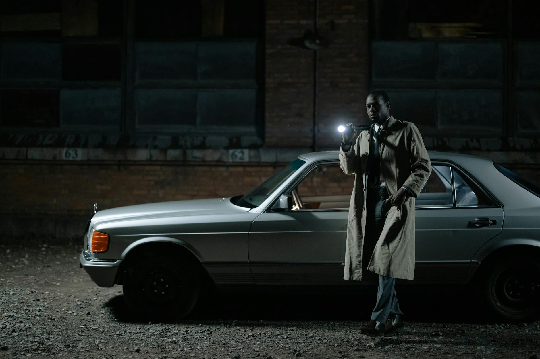 Detektyw z latarką prowadzi nocne śledztwo przy zaparkowanym samochodzie Detektyw z latarką prowadzi nocne śledztwo przy zaparkowanym samochodzie