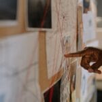 Śledczy wskazuje tablicę dowodów połączonych czerwonymi nićmi